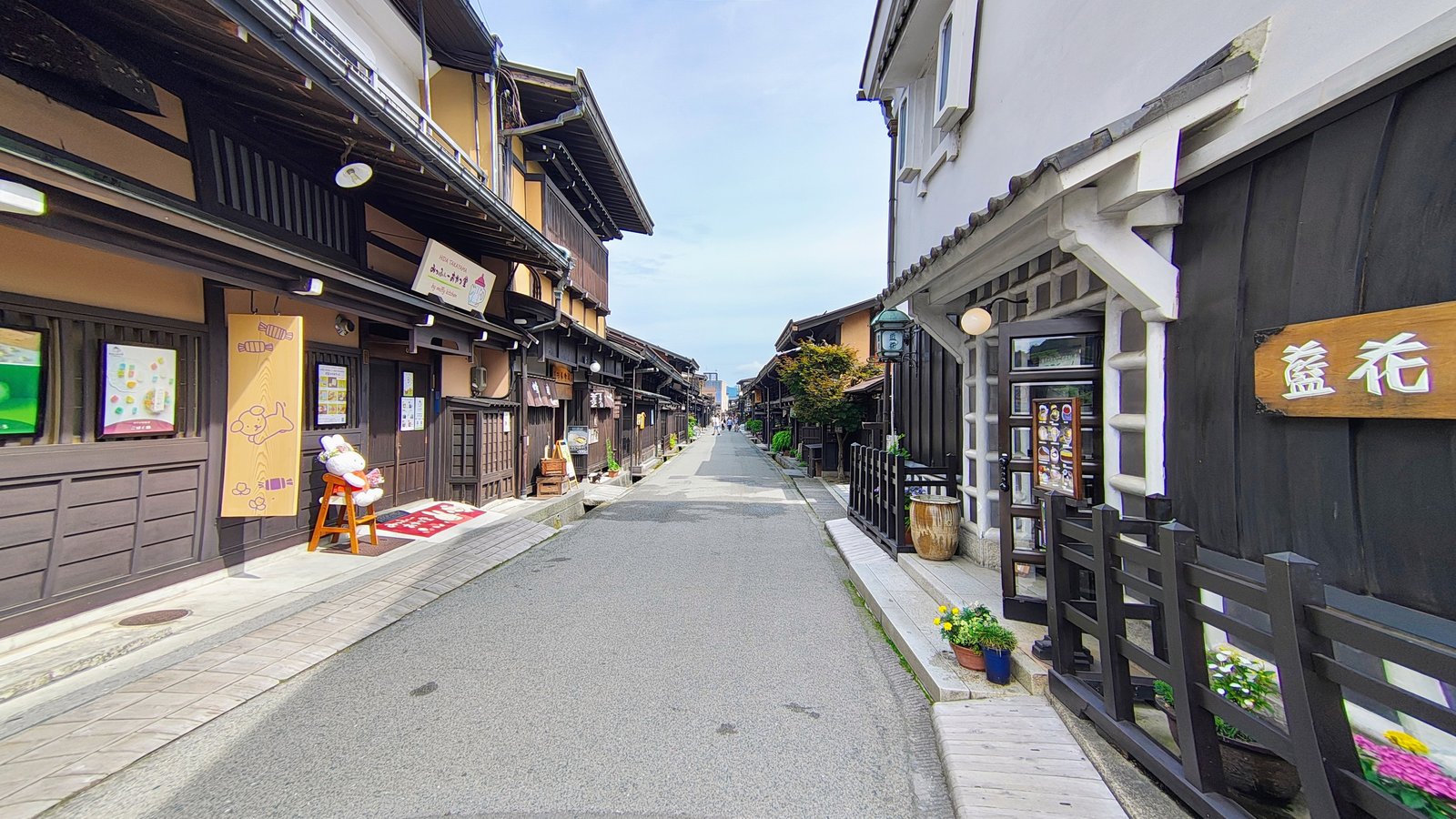 ถนนคามิซันโนมาจิในย่านเมืองเก่าทาคายาม่า อาคารไม้สีเข้มสองฝั่งกับโคมไฟและป้ายร้านไม้สีเรียบ