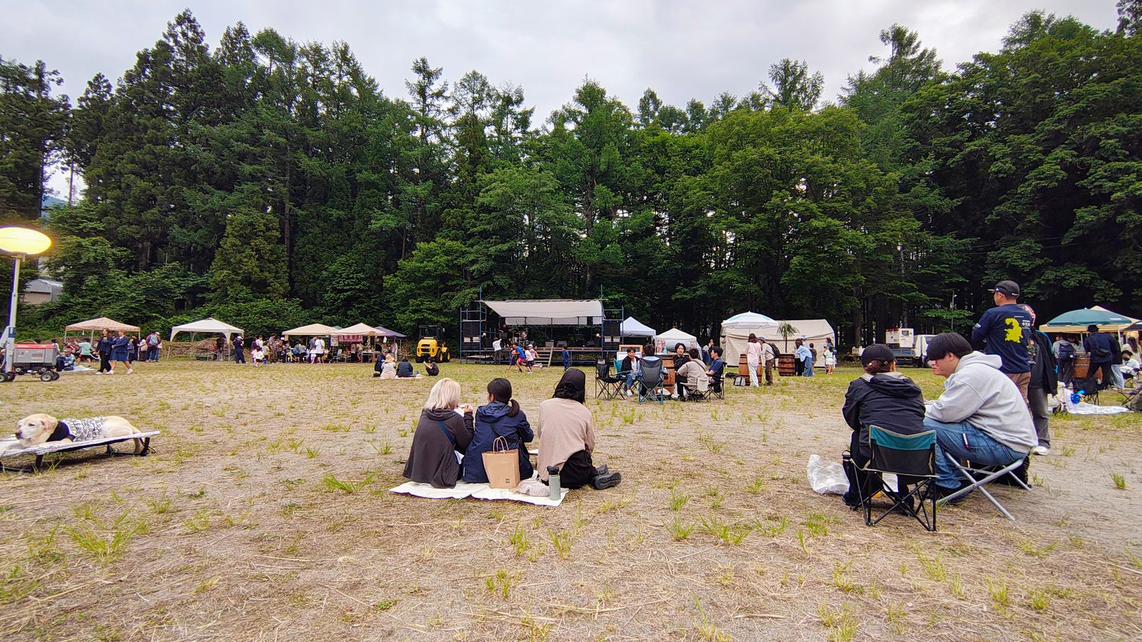ผู้คนนั่งชิลบนสนามหญ้ามองเวทีจากระยะไกล บรรยากาศปิกนิกสบาย ๆ มีน้องหมามาด้วย