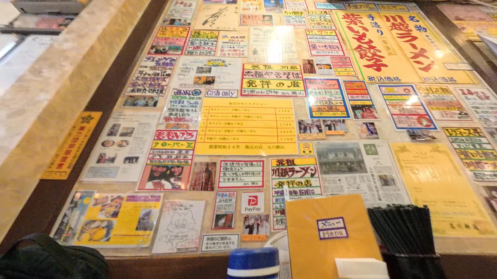 โต๊ะในร้านราเมนที่ปูเต็มไปด้วยใบปลิวและบทความที่ร้านเคยออกสื่อ